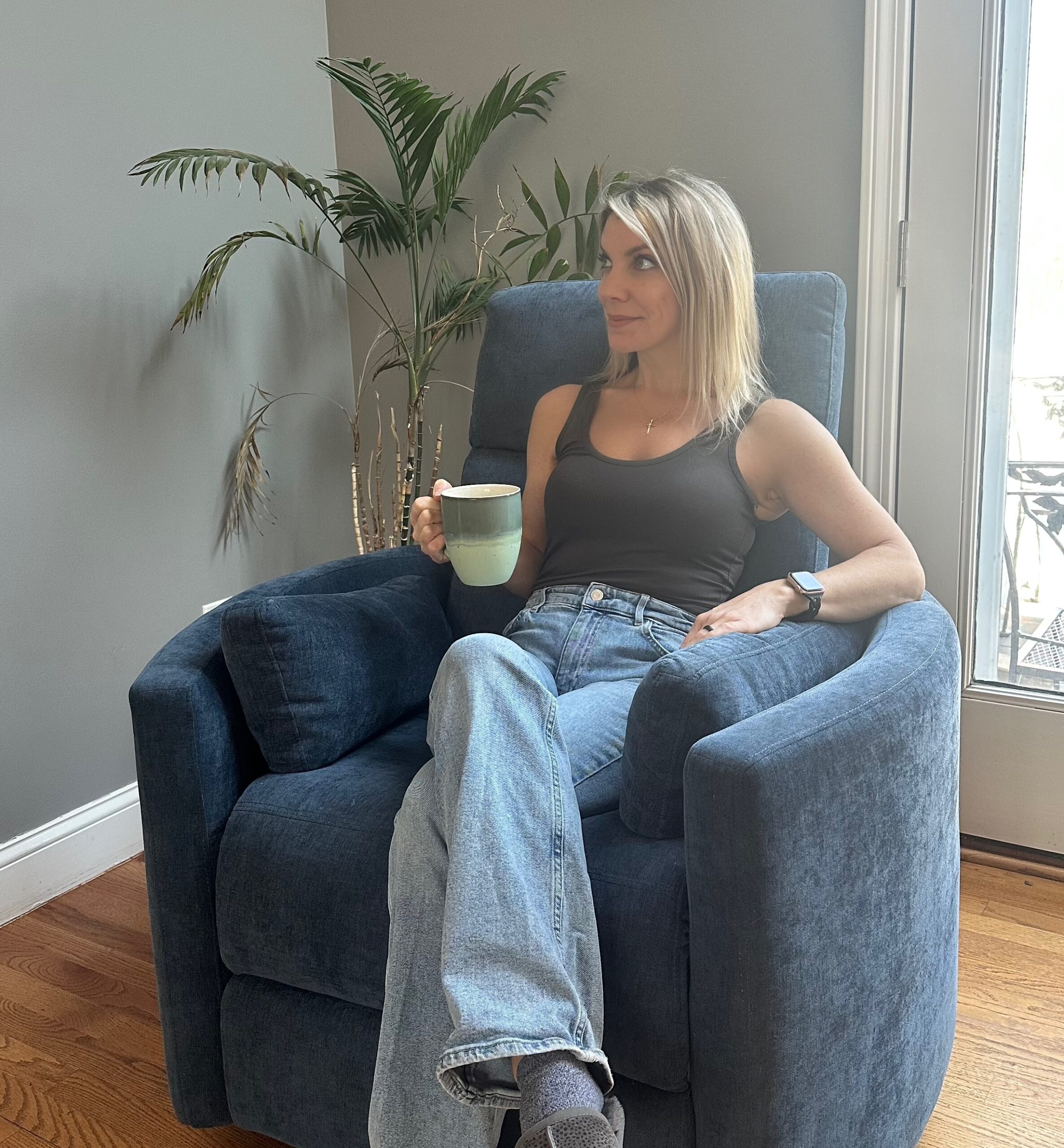 Woman relaxing with a mug in a cozy chair, looking peaceful and confident in her natural appearance.